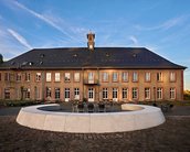 Historisches Gebäude mit einem Uhrturm, umgeben von einem runden Sitzbereich und einer gepflasterten Fläche.