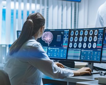 Eine Ärztin analysiert medizinische Bilder auf mehreren Bildschirmen in einem modernen Labor, während Kollegen im Hintergrund diskutieren.