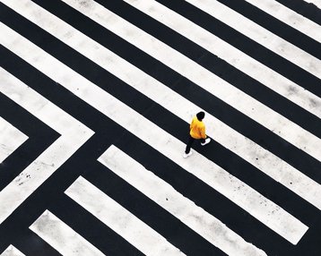 Eine Person in gelber Kleidung geht über ein geometrisches Zebrastreifenmuster aus schwarzen und weißen Linien.